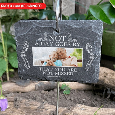 Slate hanging plaque with photo of an elderly couple and text 'Not a day goes by that you are not missed' in a garden setting.