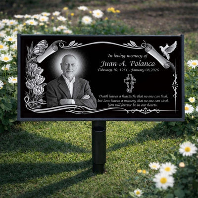 Memorial sign with a portrait of a man and engraved text in a garden setting.