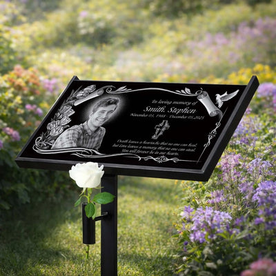 Memorial sign with a portrait of a man and engraved text in a garden setting.