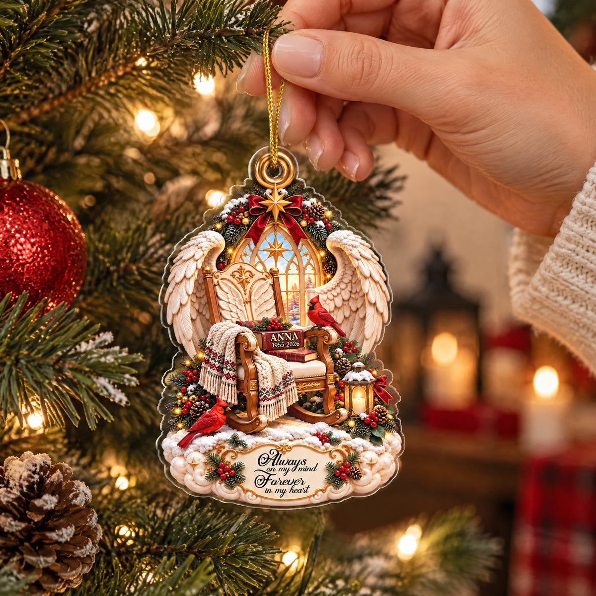 Personalized Angel Wings Memorial Acrylic Ornament held by hand near a red bauble and pine branches