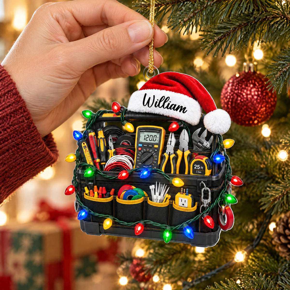 Personalized electrician tool bag acrylic ornament held by a hand in a red sleeve near a decorated tree