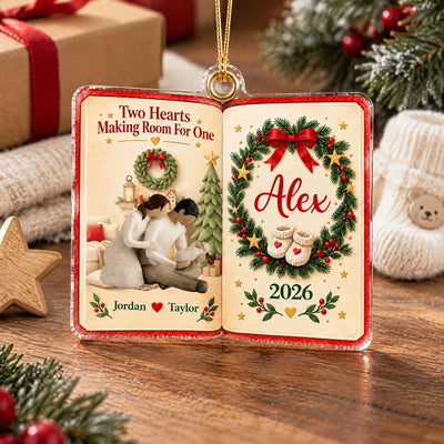 Personalized acrylic ornament Two Hearts Making Room For One standing on a wood surface with baby booties and gifts