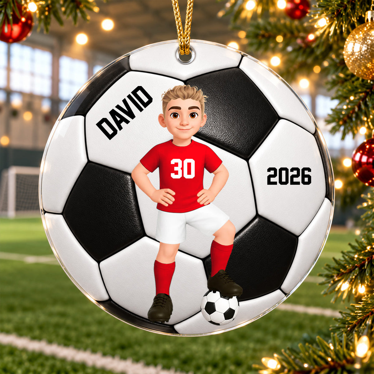 Personalized soccer acrylic ornament hanging by a gold cord near a Christmas tree with an indoor soccer field behind