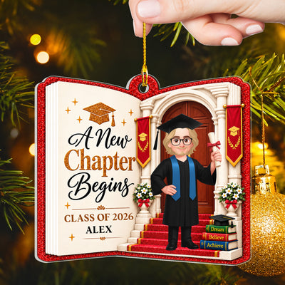 Personalized acrylic graduate ornament held up by a hand, showing a male graduate in a blue stole by a gold bauble
