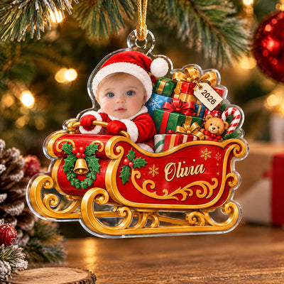 Personalized acrylic ornament baby sleigh hanging on a tree with warm lights, showing baby in Santa hat and name Olivia