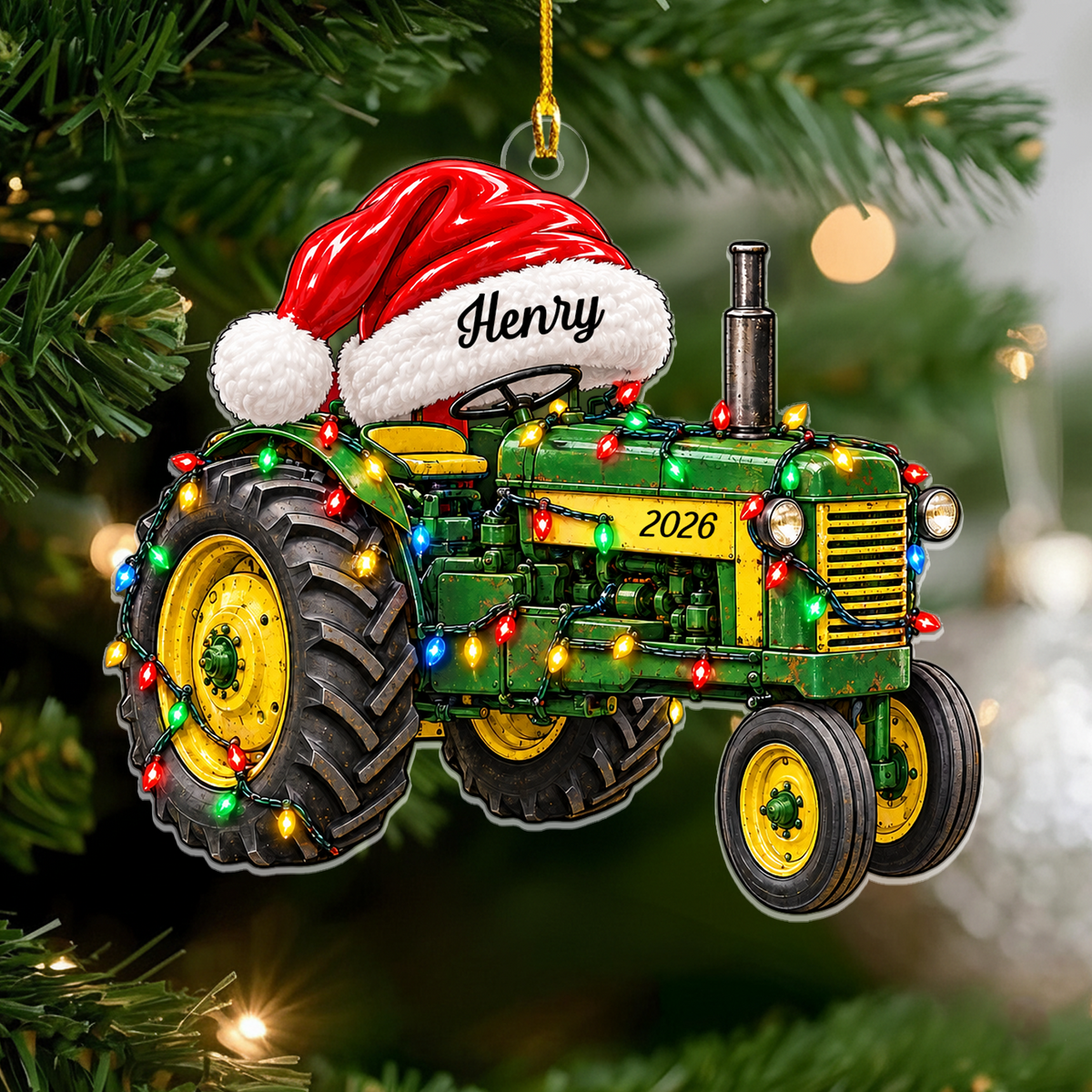 Personalized tractor acrylic ornament with Santa hat reading Henry, hanging on a pine branch with blurred lights
