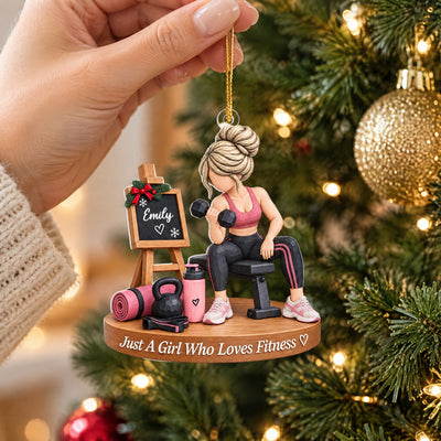 Personalized fitness girl acrylic ornament held by gold cord in a hand near gold bauble and tree lights