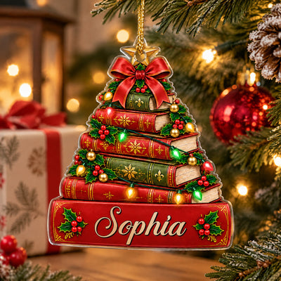 Personalized book Christmas tree acrylic ornament on a tree near a wrapped gift, pinecone and red bauble