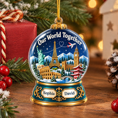 Personalized acrylic snow globe ornament standing on a wooden table beside red gift, berries and pinecone