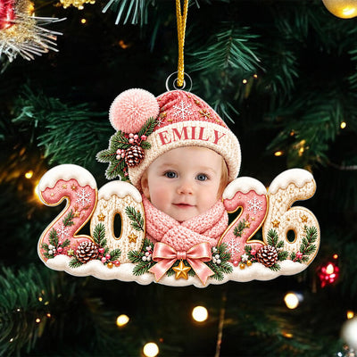Personalized Baby Photo Acrylic Ornament 2026 in pink with a baby face, knit hat and name, hanging on a dark tree