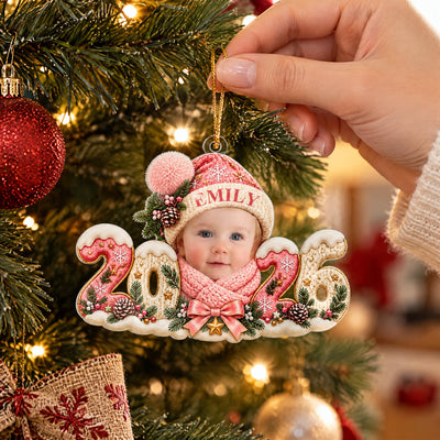 Personalized Baby Photo Acrylic Ornament 2026 held by a hand on a lit tree beside a red bauble