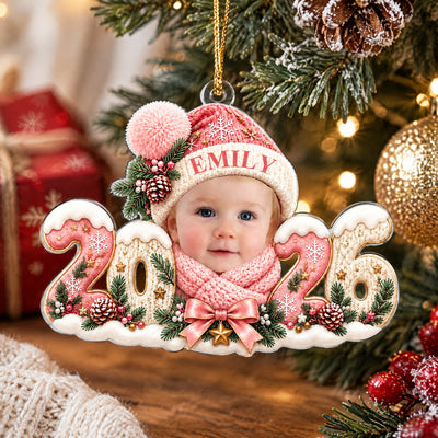 Personalized Baby Photo Acrylic Ornament 2026 in pink close up with a gold ball, pine cones and a wrapped gift behind