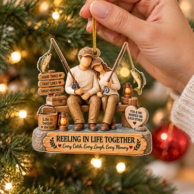 Personalized Acrylic Ornament Reeling In Life Together held by its gold cord in a hand near tree lights