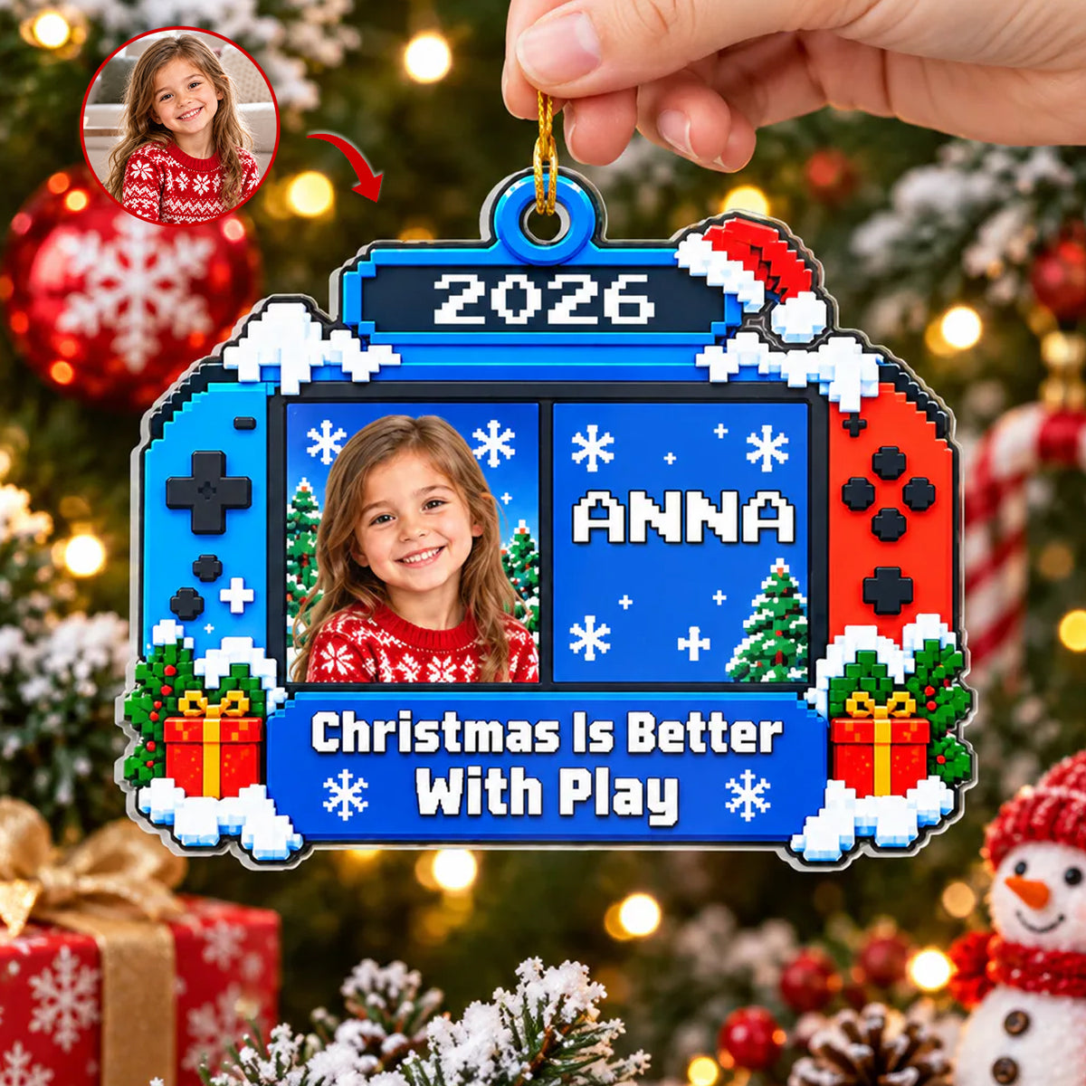 Personalized Acrylic Gamer Ornament held by a hand by its gold cord, with ornaments and a snowman in the background