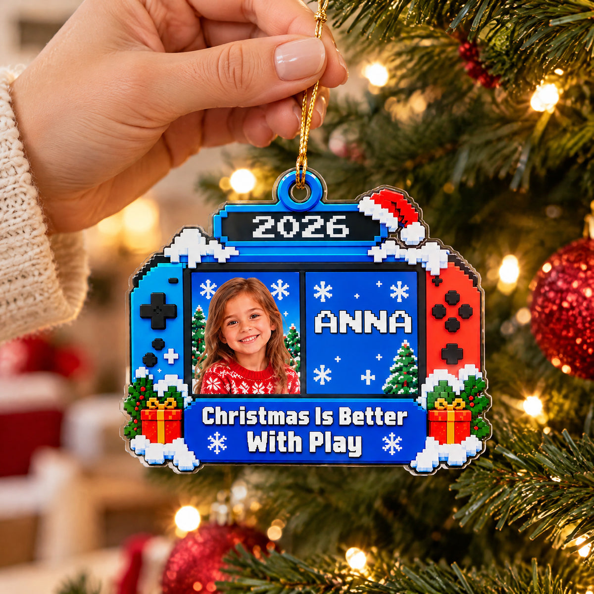 Personalized Acrylic Gamer Ornament held up close in front of a lit tree, showing a girl's photo and name Anna