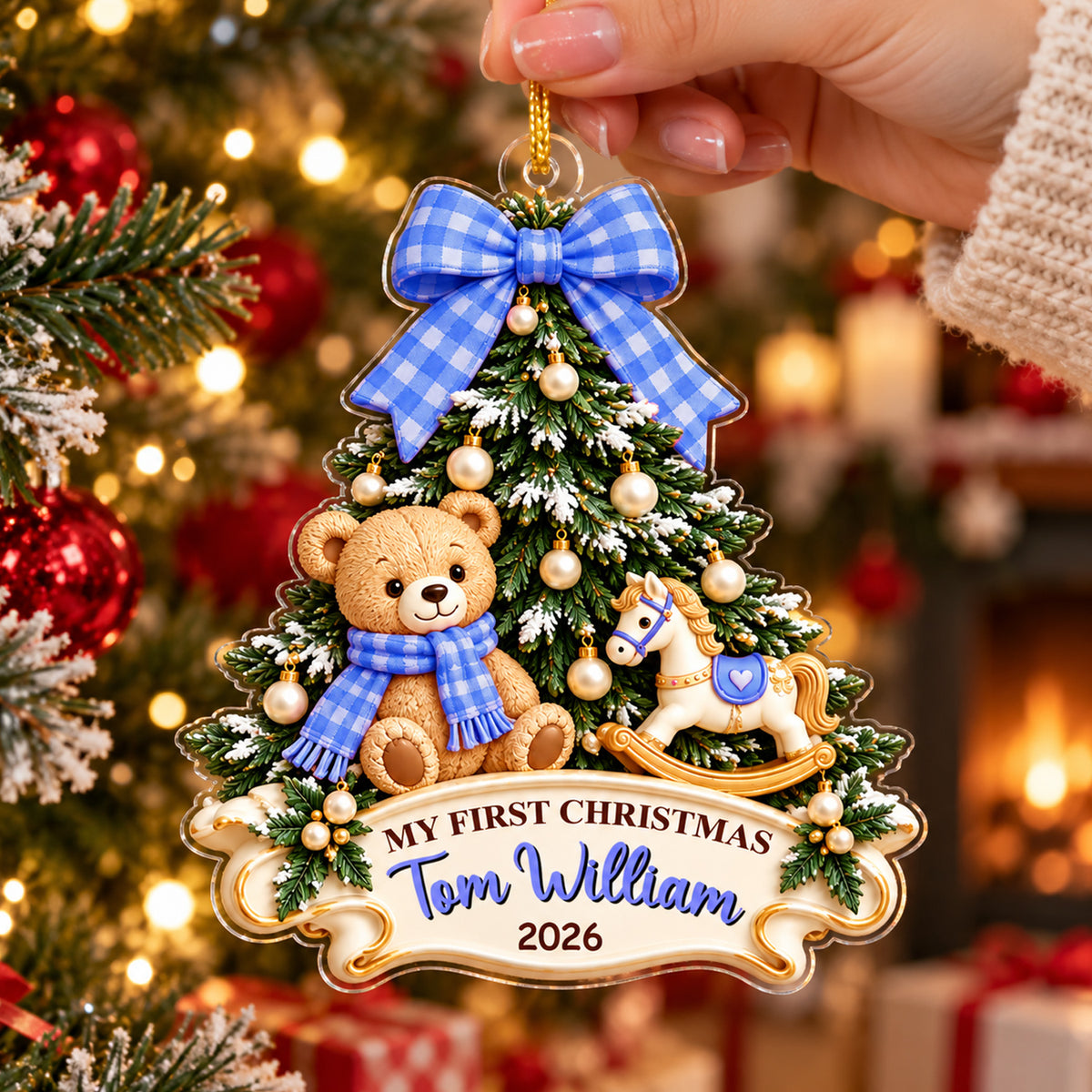 Personalized Teddy Bear Acrylic Ornament with blue bow held by a hand in front of a tree and glowing fireplace