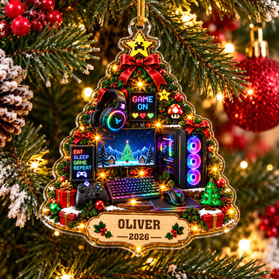 Personalized Gamer Christmas Tree Acrylic Ornament hanging on a pine branch beside red berries and a glittery red bauble