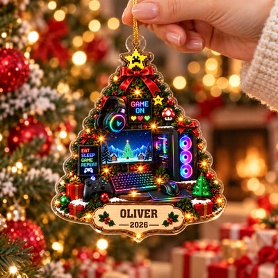Personalized Gamer Christmas Tree Acrylic Ornament held by a hand near a lit tree, with a fireplace and gifts behind