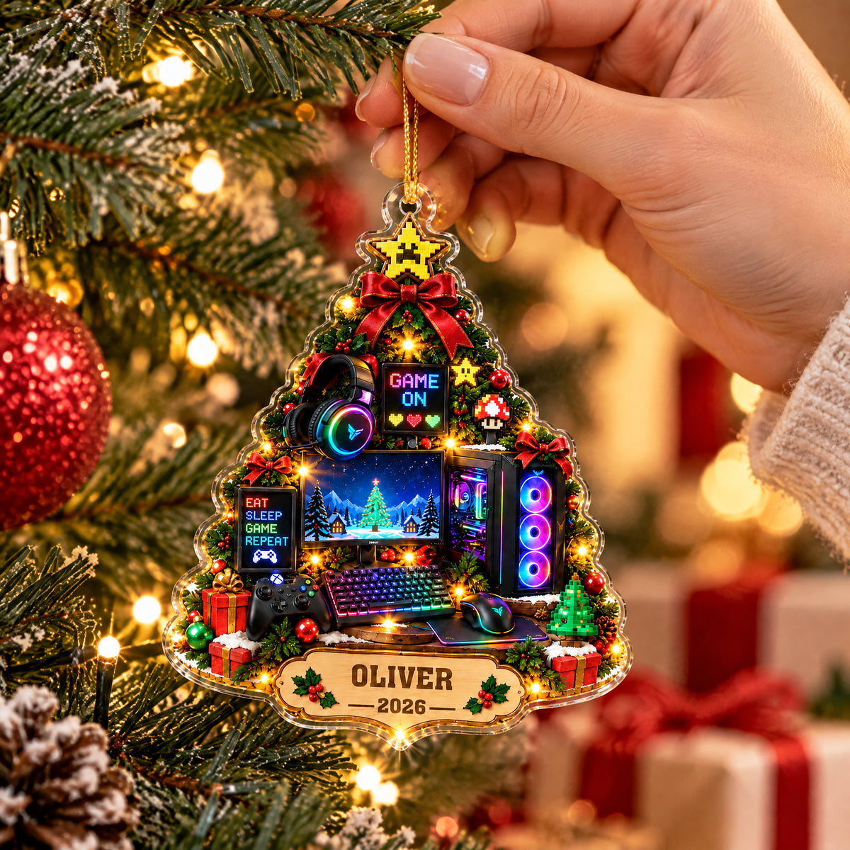 Personalized Gamer Christmas Tree Acrylic Ornament held up close by a hand in front of tree lights and red baubles