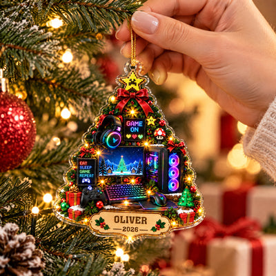 Personalized Gamer Christmas Tree Acrylic Ornament held up close by a hand in front of tree lights and red baubles