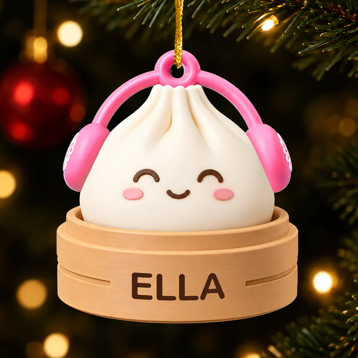 Personalized acrylic dumpling ornament with pink earmuffs and smiling face, name on steamer, hanging on a lit tree