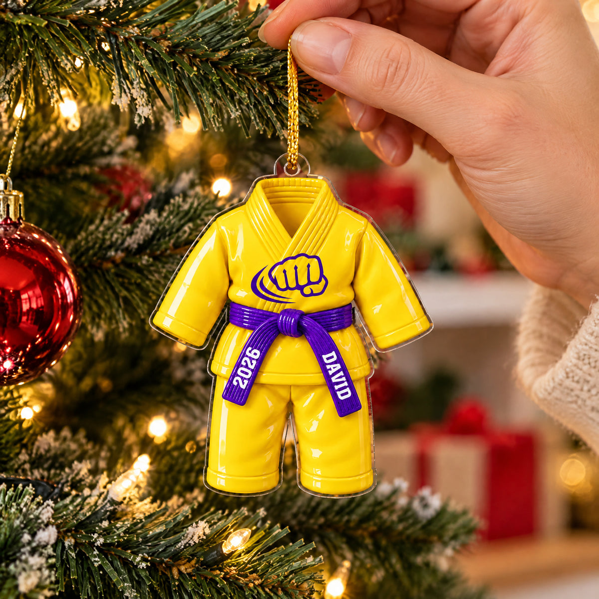 Personalized karate uniform acrylic ornament in yellow held by a hand beside red bauble on a Christmas tree