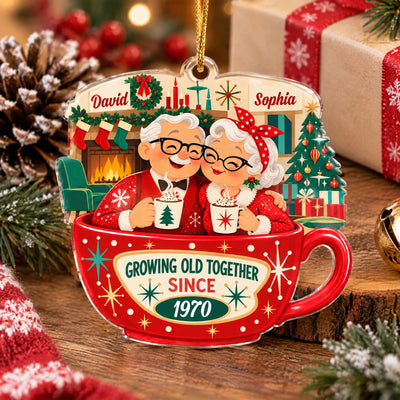 Personalized Christmas acrylic ornament resting on a wood slice beside a pine cone, wrapped gift and a gold bell