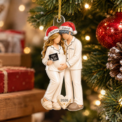 Personalized Pregnancy Christmas Acrylic Ornament on a tree beside a pinecone, red gift boxes behind