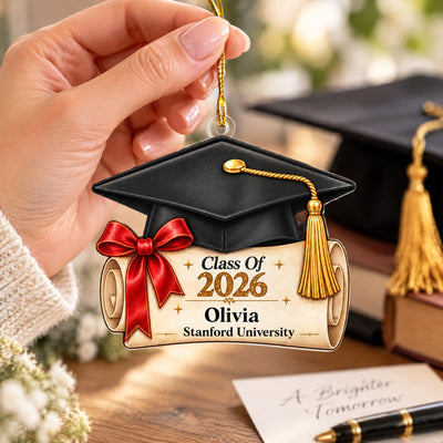 Personalized graduation cap acrylic ornament held in a hand near books, a pen and a handwritten card
