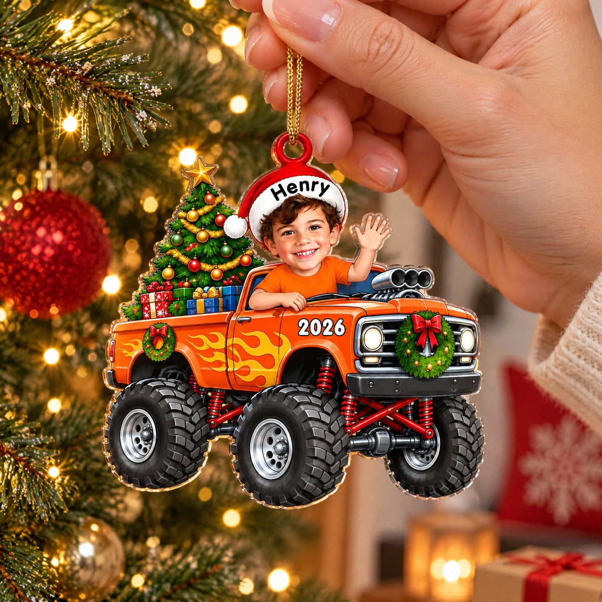 Personalized orange monster truck acrylic ornament hanging from a gold cord beside tree lights and a red bauble