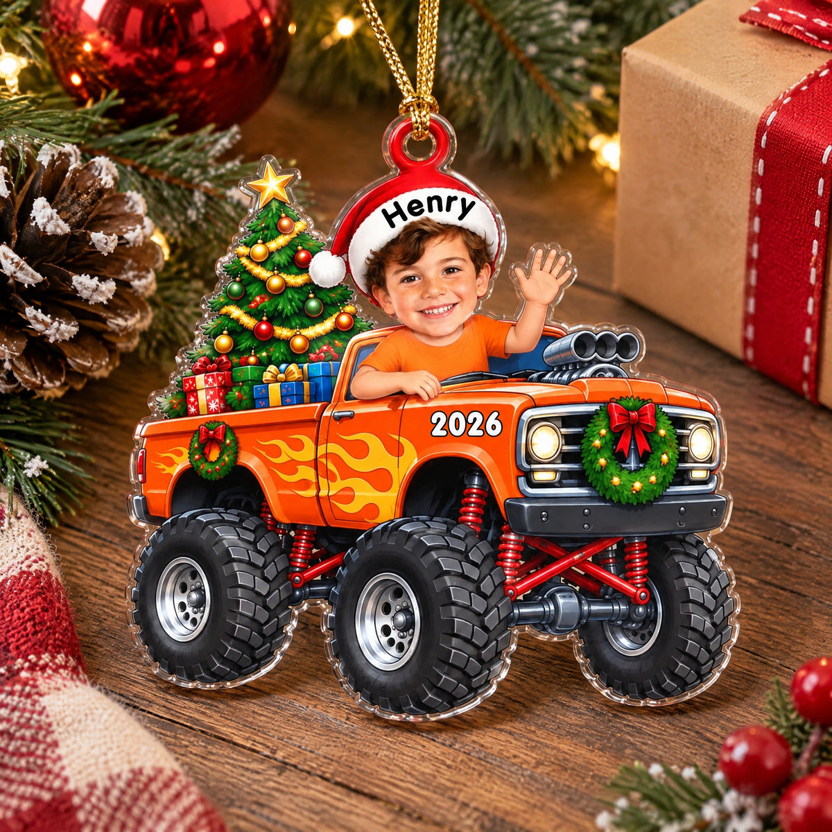 Personalized orange monster truck acrylic ornament lying on a wooden table with a wrapped gift and pinecone