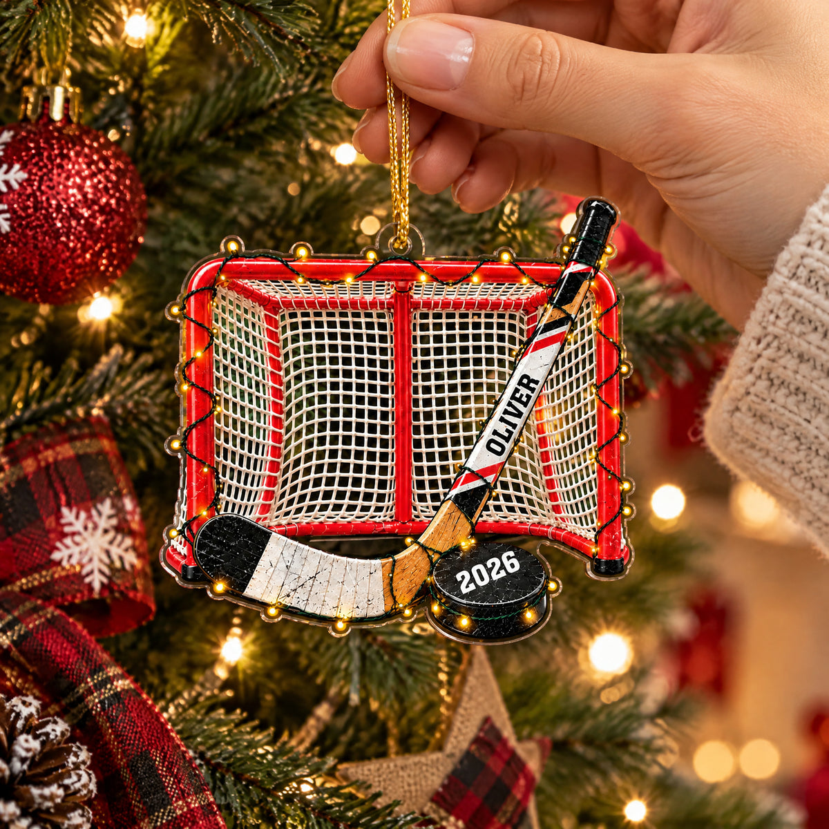 Personalized Acrylic Hockey Ornament held by a hand in a knit sleeve, plaid ribbon and tree lights behind