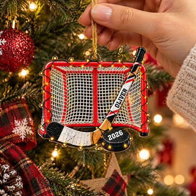 Personalized Acrylic Hockey Ornament held by a hand in a knit sleeve, plaid ribbon and tree lights behind