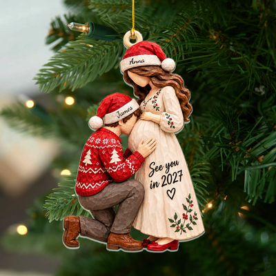 Personalized Acrylic Christmas Ornament showing a kneeling man kissing a pregnant woman's belly, hanging on a green tree