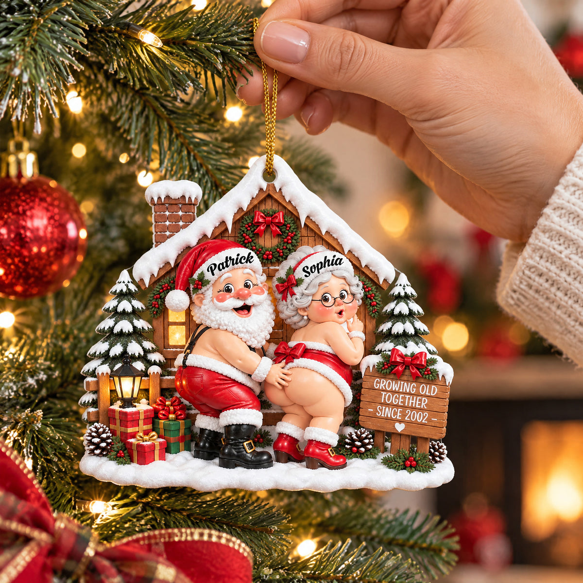 Personalized Acrylic Ornament Santa Couple held by a hand on a gold cord near tree and fireplace glow