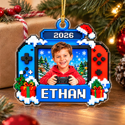 Personalized Pixel Game Console Acrylic Ornament standing on a wooden table beside a wrapped gift and pinecone
