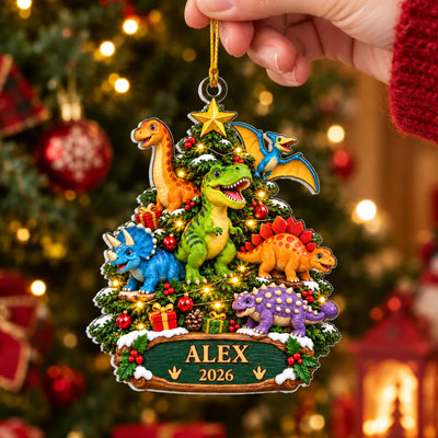 Personalized acrylic dinosaur ornament reading Alex 2026 held up by a hand in front of a lit Christmas tree