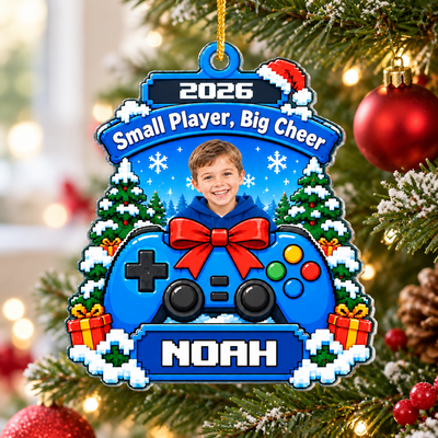 Personalized acrylic gamer ornament hanging on a Christmas tree beside a red bauble, showing a boy's photo and name