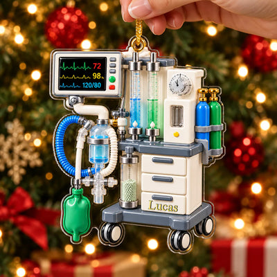 Personalized anesthesia machine acrylic ornament held by hand in front of a lit tree, name Lucas on the drawer