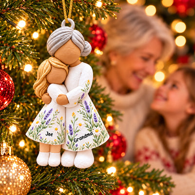 Personalized Grandmother And Granddaughter Acrylic Ornament hugging on red velvet beside a gift with red ribbon