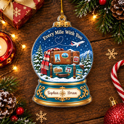 Personalized acrylic snow globe ornament lying on a wooden table with candle, candy cane, pinecones and snowflakes