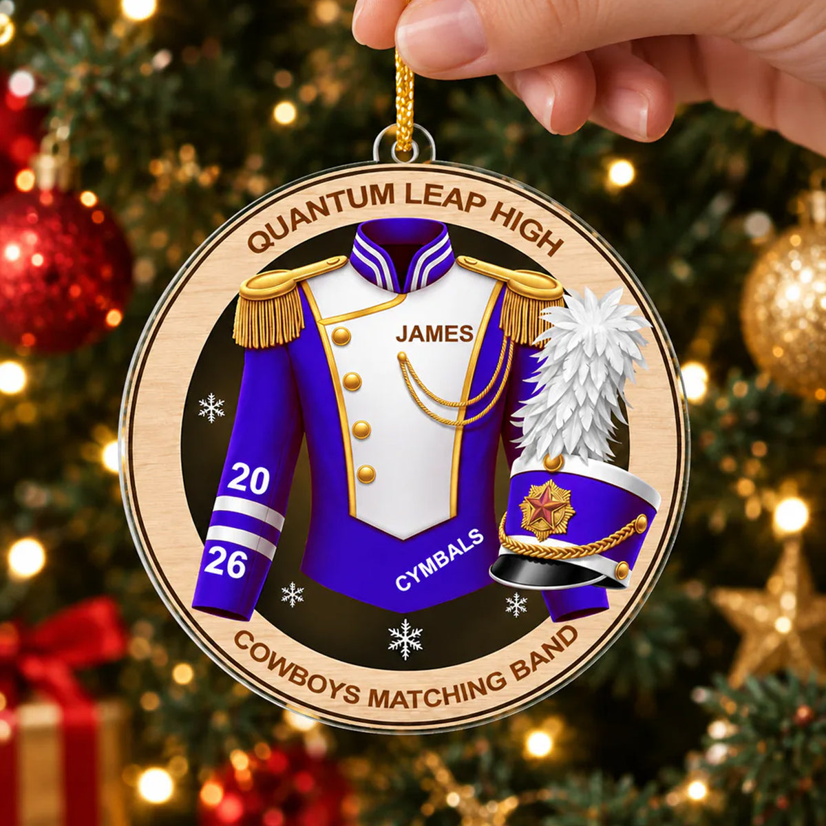 Personalized marching band acrylic ornament in purple held by hand near a lit Christmas tree with red and gold baubles