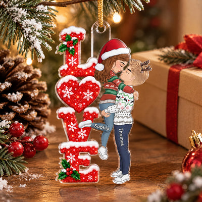 Personalized Acrylic Ornament Kissing Couple hung beside a wrapped gift, pinecone and red berries, names Sophia and Thomas