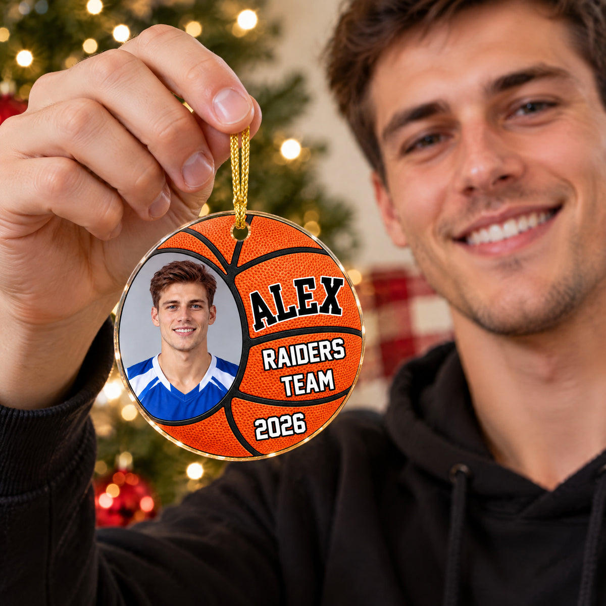 Personalized basketball acrylic ornament held up by a smiling man in a black hoodie near a Christmas tree