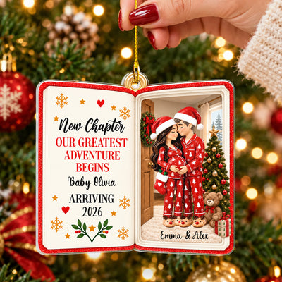 Personalized acrylic book ornament held by a hand with red nails in front of a lit Christmas tree, red pajama couple