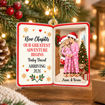 Personalized acrylic book ornament held by a hand with red nails in front of a lit Christmas tree, red pajama couple