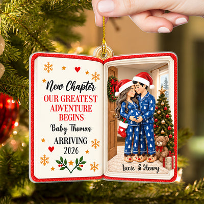 Personalized acrylic book ornament with blue pajama couple held by fingertips against a Christmas tree and red bauble