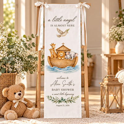 Personalized Baby Shower Backdrop hanging on a wooden easel with ribbon bows, teddy bear, flowers and a lantern nearby