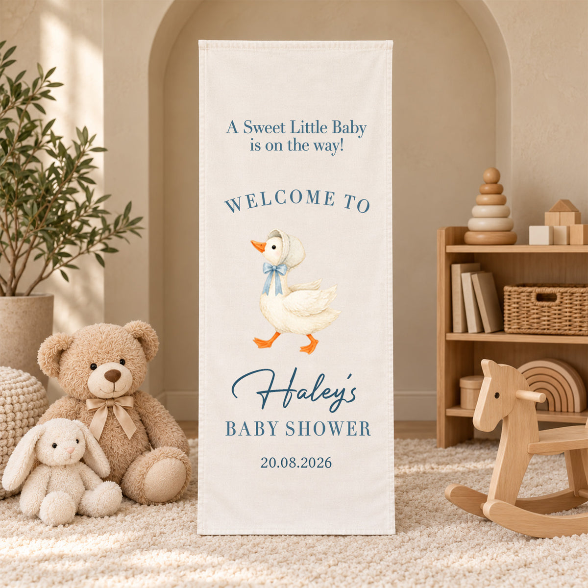 Personalized Baby Shower Welcome Sign Backdrop with goose in blue bow, standing by a rocking horse and toy shelf