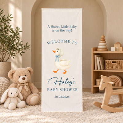Personalized Baby Shower Welcome Sign Backdrop with goose in blue bow, standing by a rocking horse and toy shelf